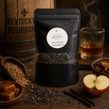 A black stand-up pouch of Kentucky Bourbon loose-leaf tea with a white circular label reading 'Southern Roots Spice' and 'Kentucky Bourbon,' placed on a rustic wooden table with bourbon, an apple, cinnamon sticks, and sugar bowls around it.